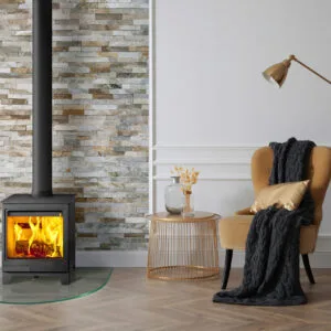 A modern wood stove with flames, a cozy chair, and a decorative lamp in a stylish interior setting, featuring a stone wall.