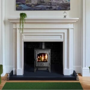Black multifuel stove placed within a white fireplace, surrounded by a green rug and modern decor.