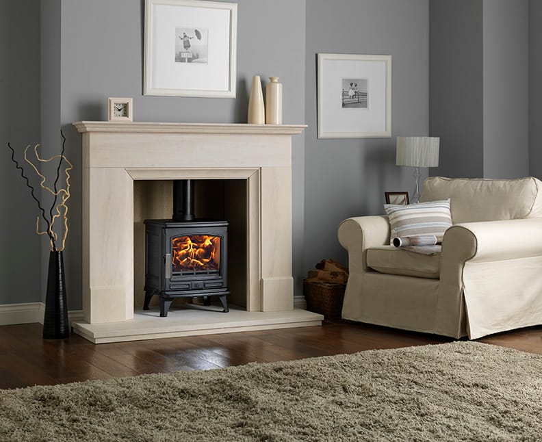 ACR Oakdale 5kW multi-fuel stove burning in a traditional living room fireplace beside a cream armchair