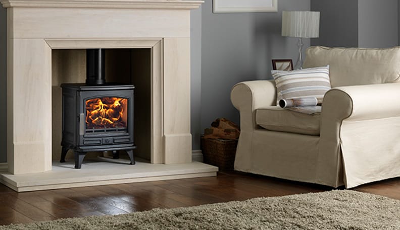 ACR Oakdale 5kW multi-fuel stove burning brightly in a traditional fireplace beside a cream armchair and wood flooring
