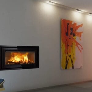 A Lotus H570W Wide Black Magic inset stove burns brightly within a black rectangular surround in a modern living room.