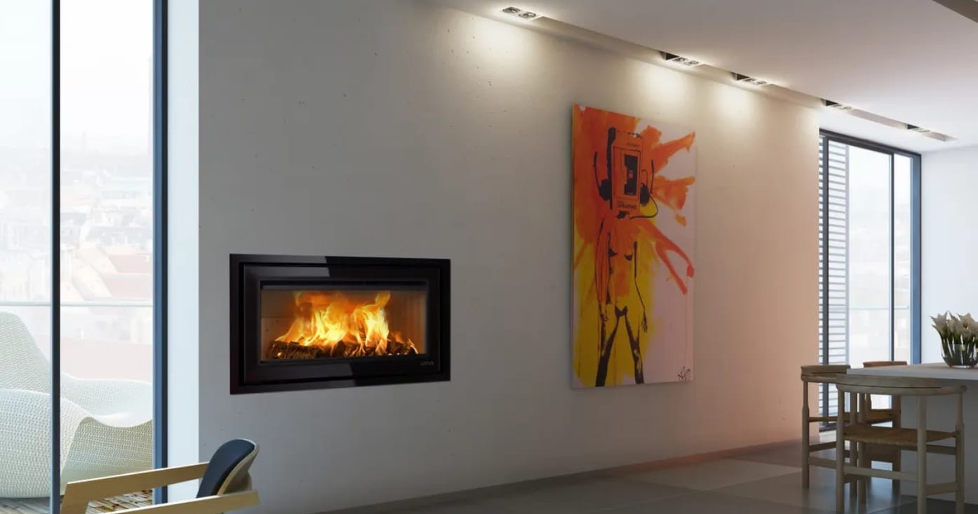 Flames burn behind the glass of a Lotus H570W Wide Black Magic inset stove set into a pale wall in a modern living room.